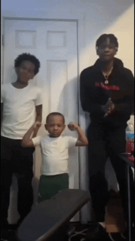 A Young Boy Flexes His Muscles While Standing Next To Two Men GIF