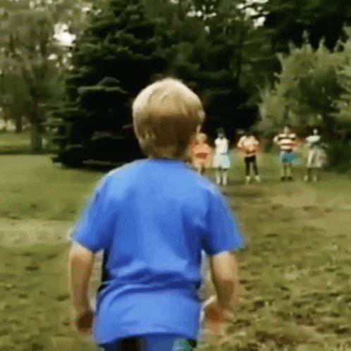 A Young Boy In A Blue Shirt Is Running Towards A Group Of Children In A Park . GIF