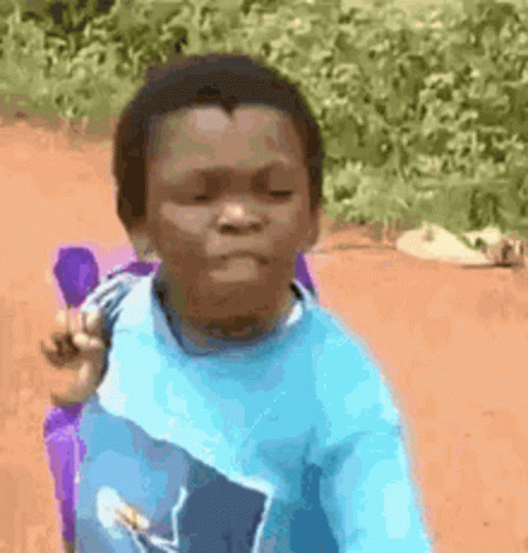 A Young Boy In A Blue Shirt Is Sitting On A Dirt Road With A Purple Backpack . GIF
