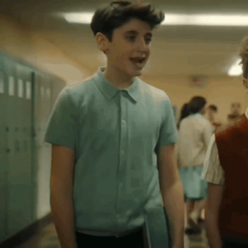 a young boy in a blue shirt is walking down a hallway with other children .