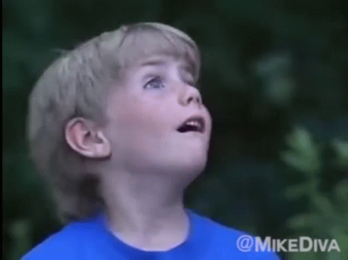 A Young Boy In A Blue Shirt Looks Up At The Sky GIF