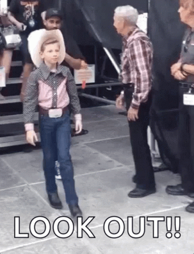 A Young Boy In A Cowboy Outfit Is Walking On A Stage While Talking To A Man . GIF
