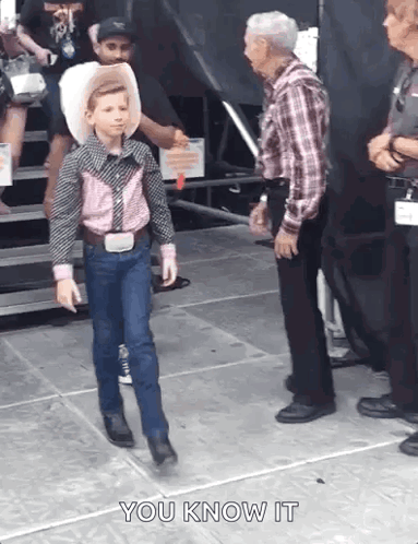 A Young Boy In A Cowboy Outfit Is Walking Towards A Man In A Plaid Shirt . GIF