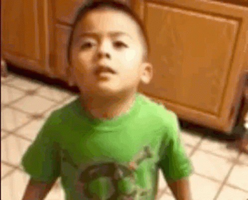 A Young Boy In A Green Shirt Is Standing On A Tiled Floor . GIF