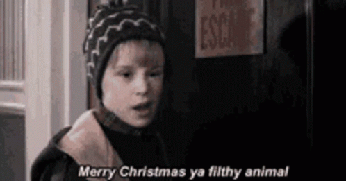A Young Boy In A Hat Is Standing In Front Of A Door And Says `` Merry Christmas Ya Filthy Animal '' . GIF