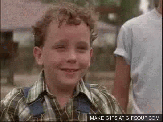 A Young Boy In A Plaid Shirt And Overalls Is Smiling . GIF
