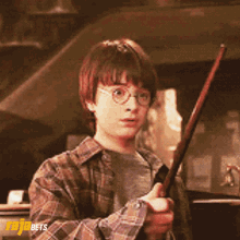 A Young Boy In A Plaid Shirt Is Holding A Wand In His Hand GIF