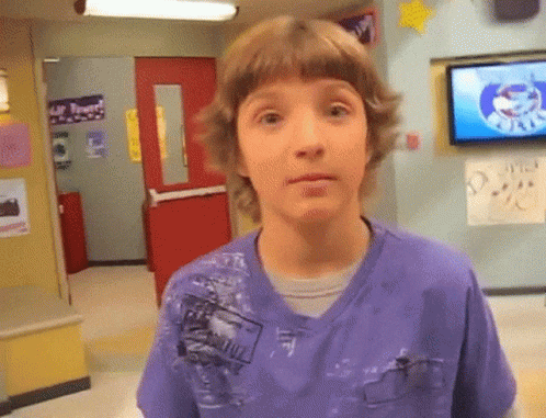 A Young Boy In A Purple Shirt Is Standing In Front Of A Tv In A Hallway GIF