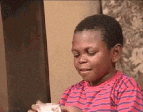 A Young Boy In A Red And Purple Striped Shirt Is Holding A Piece Of Paper In His Hand . GIF