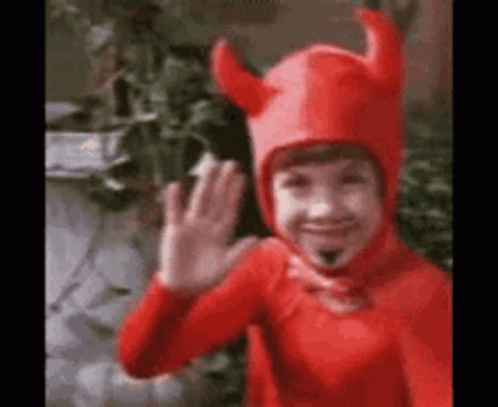 A Young Boy In A Red Devil Costume Is Waving . GIF