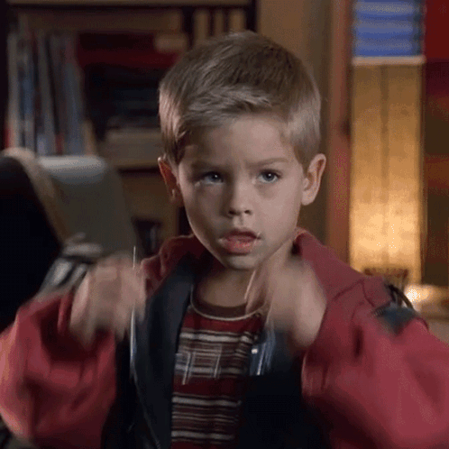 A Young Boy In A Red Jacket And Striped Shirt Is Making A Funny Face GIF