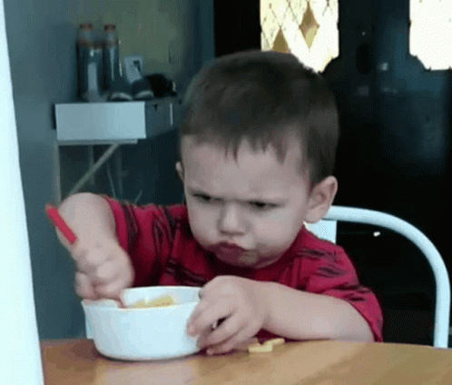 A Young Boy In A Red Shirt Is Eating Cereal With A Spoon GIF