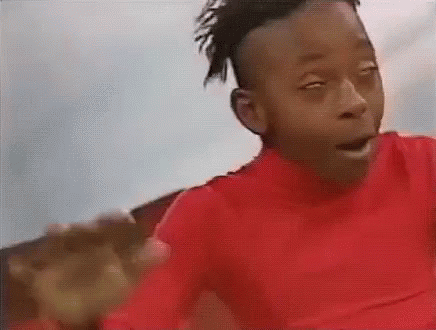A Young Boy In A Red Shirt Is Making A Funny Face While Looking At The Camera . GIF