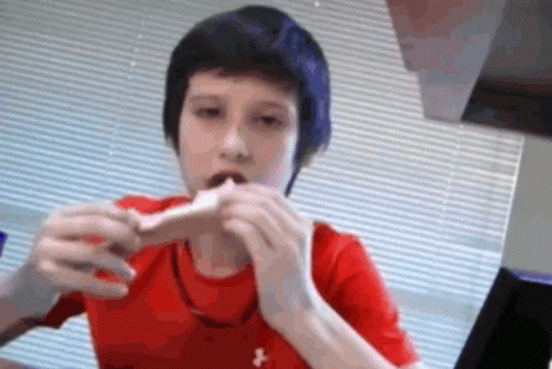 A Young Boy In A Red Under Armour Shirt Is Eating A Sandwich GIF