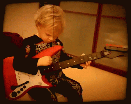 a young boy in a skeleton costume is playing a red electric guitar