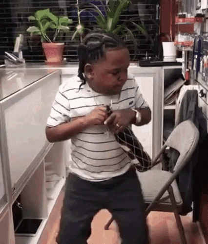 A Young Boy In A Striped Shirt Is Dancing In A Kitchen Next To A Chair . GIF