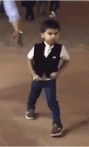A Young Boy In A Suit And Vest Is Dancing On A Stage . GIF