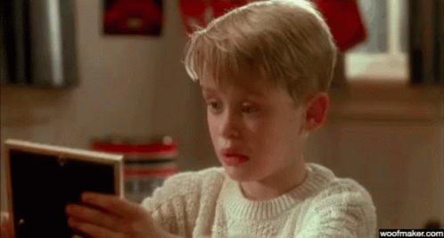 A Young Boy In A Sweater Is Looking At A Picture In A Frame . GIF