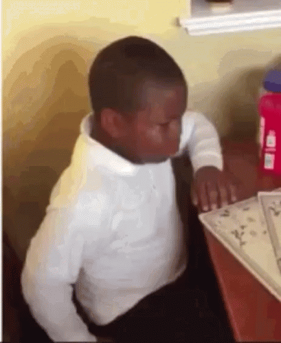 A Young Boy In A White Shirt And Tie Is Sitting At A Table With His Eyes Closed . GIF