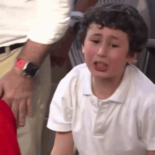 A Young Boy In A White Shirt Is Crying While A Man Holds His Arm . GIF