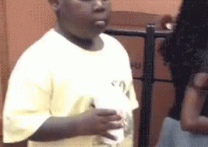 A Young Boy In A White Shirt Is Holding A Cup Of Milkshake . GIF