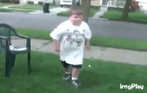 A Young Boy In A White Shirt Is Walking On A Sidewalk . GIF