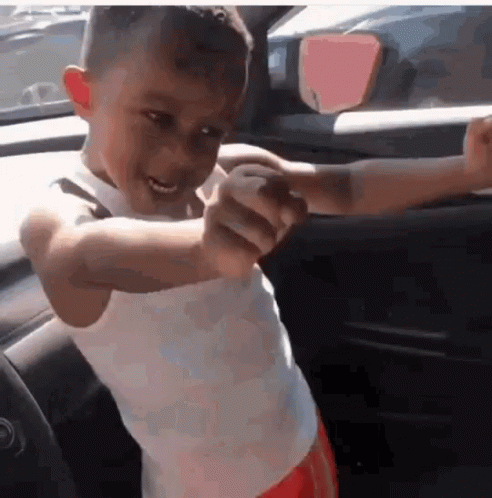 A Young Boy In A White Tank Top Is Standing In A Car With His Arms Outstretched GIF