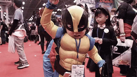 A Young Boy In A Wolverine Costume Is Standing In A Crowd . GIF