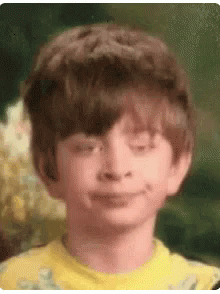 A Young Boy In A Yellow Shirt Is Smiling With His Eyes Closed . GIF
