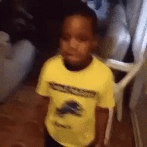 A Young Boy In A Yellow Shirt Is Standing In A Hallway . GIF