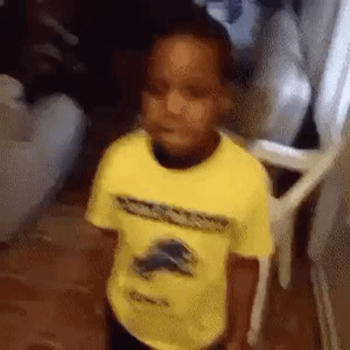 A Young Boy In A Yellow Shirt Is Standing In A Room . GIF