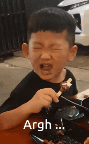 A Young Boy Is Eating A Skewer Of Food And The Word Argh Is On The Bottom GIF