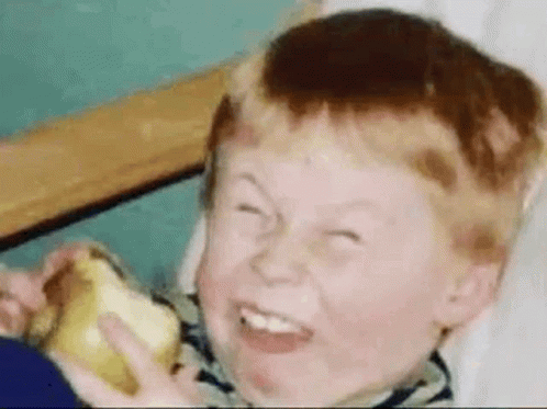 A Young Boy Is Eating An Apple And Making A Funny Face . GIF