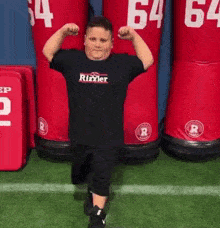 A Young Boy Is Flexing His Muscles In Front Of A Row Of Red Mannequins With The Number 64 On Them GIF