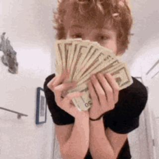A Young Boy Is Holding A Fan Of Money In Front Of His Face . GIF