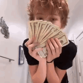 A Young Boy Is Holding A Fan Of Money In His Hands . GIF