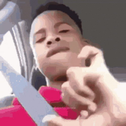 A Young Boy Is Holding A Knife In His Hand And Looking At The Camera . GIF