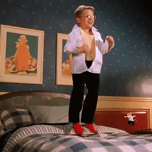 A Young Boy Is Jumping On A Bed With His Shirt Off GIF