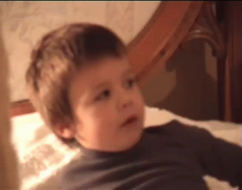 A Young Boy Is Laying On A Bed And Making A Face . GIF