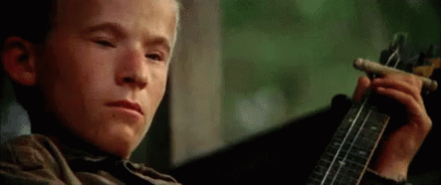 A Young Boy Is Playing A Guitar While Smoking A Cigar . GIF