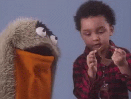 A Young Boy Is Playing With A Puppet While Holding A Piece Of Paper . GIF