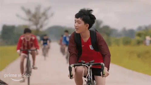 A Young Boy Is Riding A Bike Down A Dirt Road With Other People . GIF