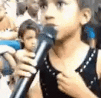 A Young Boy Is Singing Into A Microphone In A Crowd . GIF