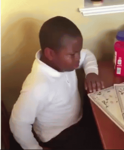 A Young Boy Is Sitting At A Desk With A Bottle Of Vaseline On It GIF
