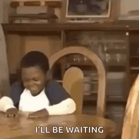 A Young Boy Is Sitting At A Table And Smiling While Waiting For Something . GIF