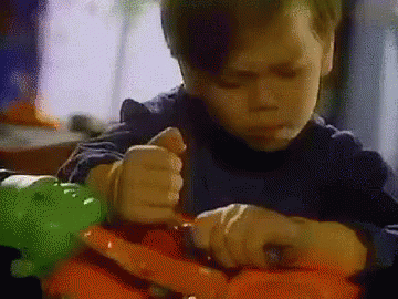 A Young Boy Is Sitting At A Table Playing With A Toy Dinosaur . GIF