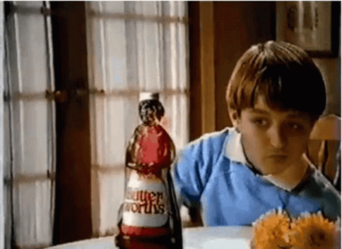 a young boy is sitting at a table with a bottle of butterworth 's ketchup .