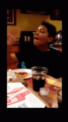 A Young Boy Is Sitting At A Table With A Cup Of Soda GIF