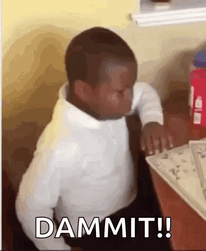 A Young Boy Is Sitting At A Table With His Eyes Closed And The Word Dammit Written On The Screen . GIF