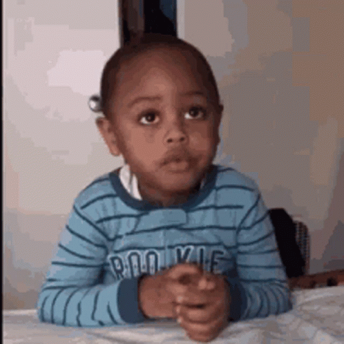 A Young Boy Is Sitting At A Table With His Hands Folded In Front Of Him . GIF